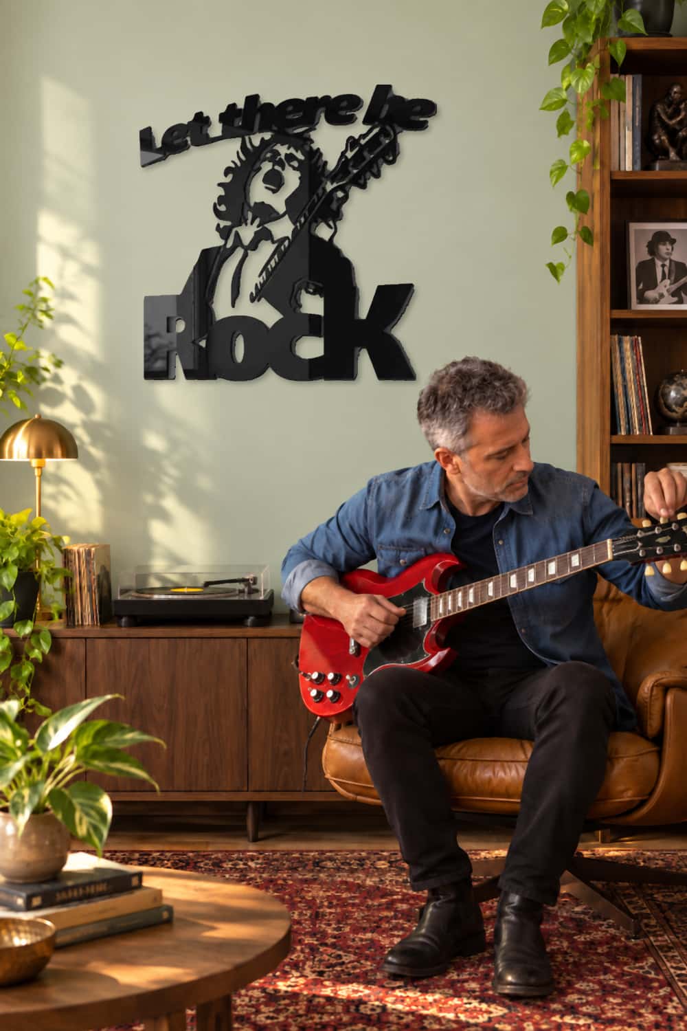 Angus Young AC/DC sobre pared salvia clara junto a un aficionado afinando su guitarra