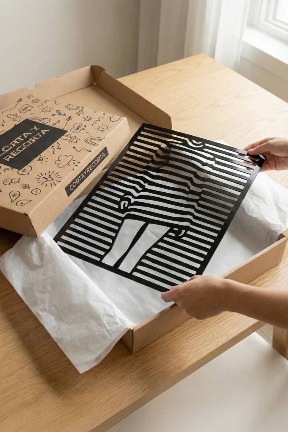 Cuadro Chica Pop de aluminio negro saliendo de su caja de envío Corta y Recorta