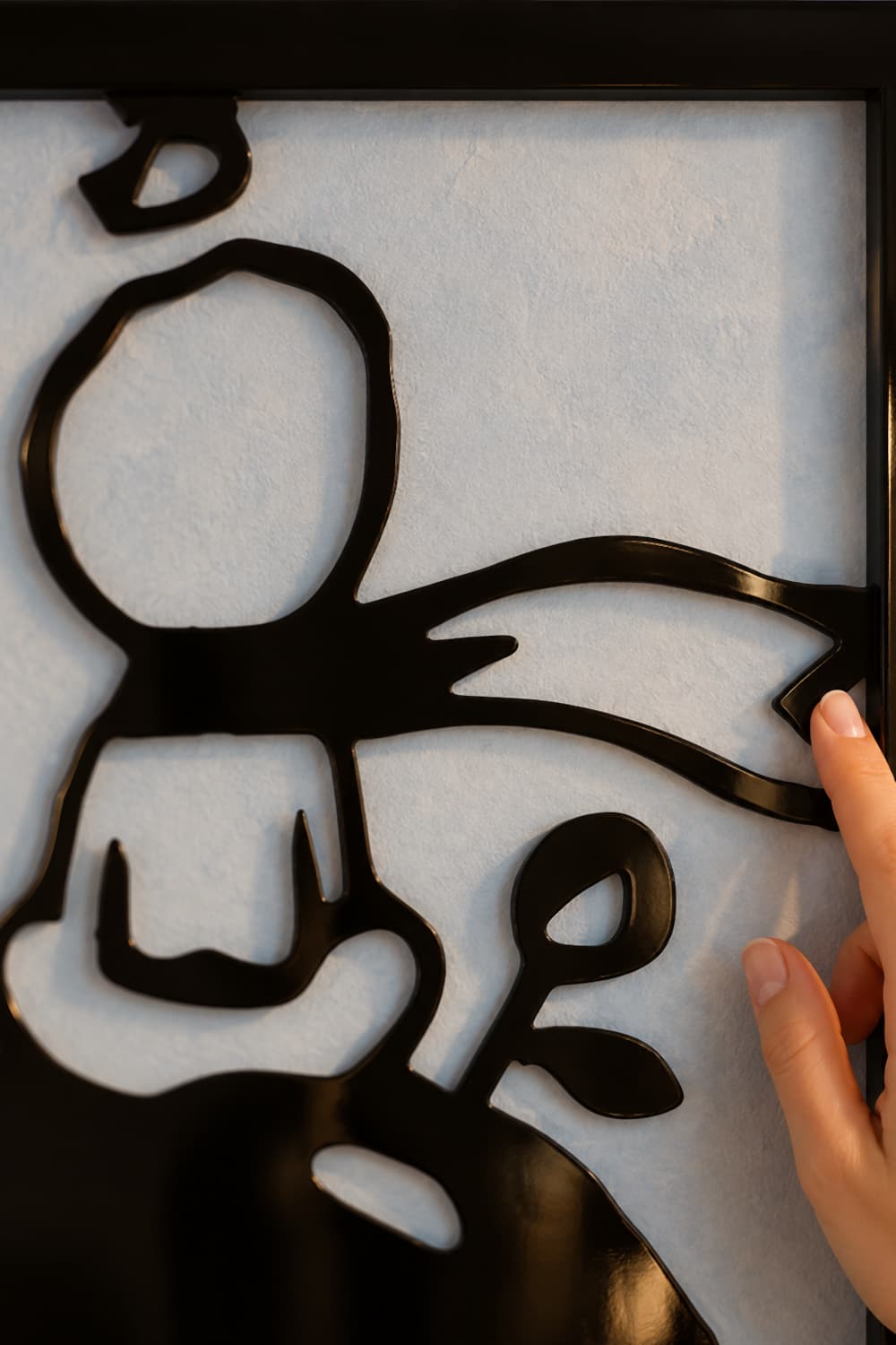 Detalle del cuadro El Principito: bufanda y rosa en aluminio negro lacado brillante y una mano que lo toca