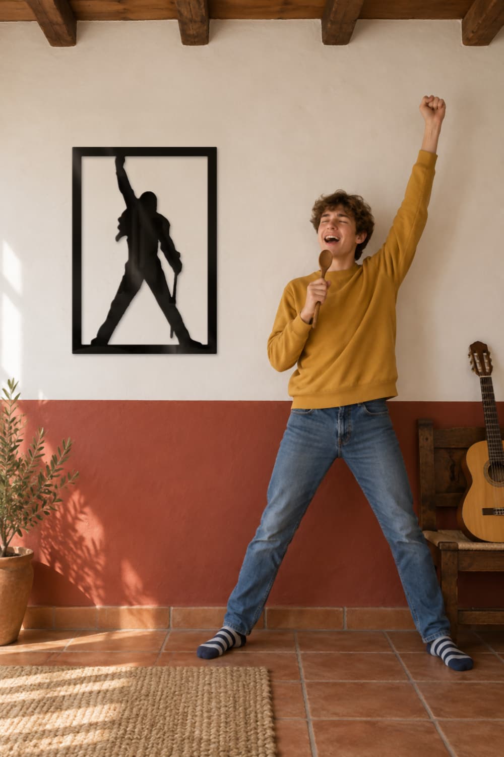 Cuadro Freddie Mercury de metal en una pared encalada mientras un joven imita su pose cantando con una cuchara