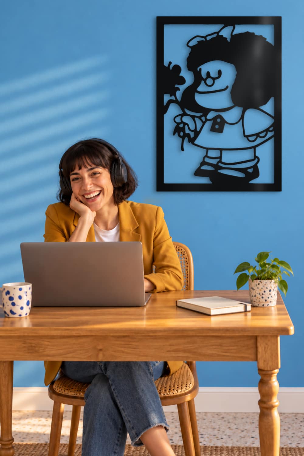Cuadro Mafalda de metal en despacho azul, mujer con cascos trabajando con su portátil