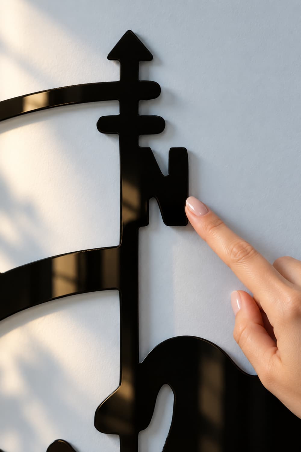 Detalle del Mapa de los Vientos: dedo sobre la N de la rosa de los vientos en aluminio negro brillante