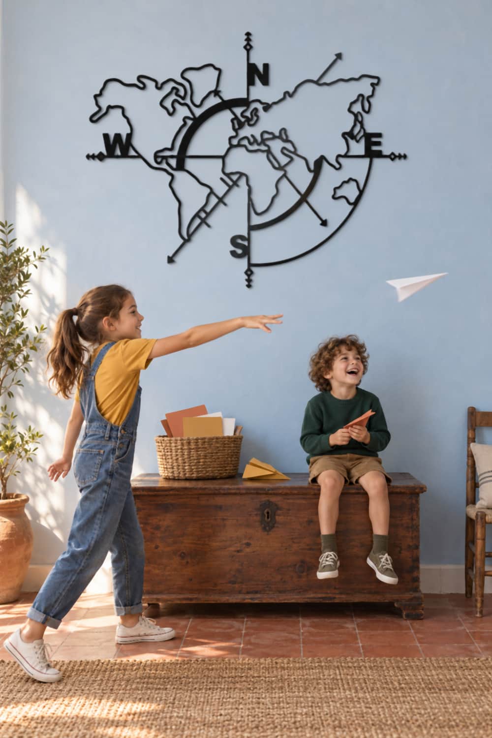 Mapa Mundi de metal negro en una pared azulete: dos hermanos lanzan aviones de papel junto a un arcón