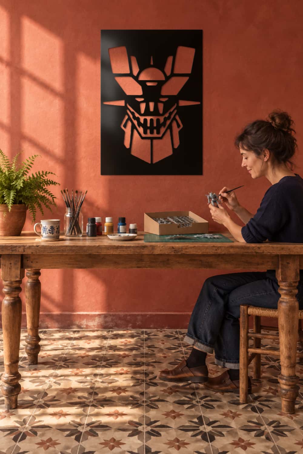 Cuadro Mazinger Z en pared almagra sobre mesa de modelismo: mujer pinta una figura de robot