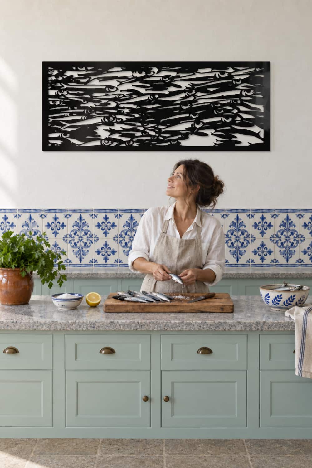 Cuadro Sardinetas en una cocina gallega con azulejos azules; una mujer limpia sardinas y lo mira