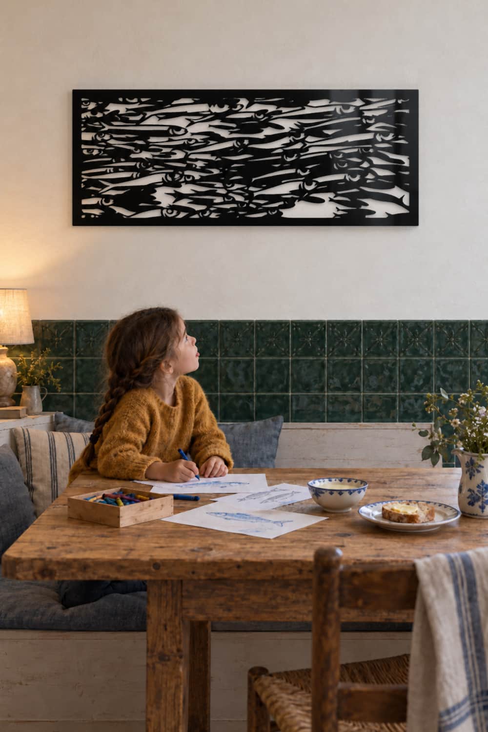Cuadro Sardinetas sobre azulejo verde en un rincón de cocina; una niña dibuja sardinas y lo mira