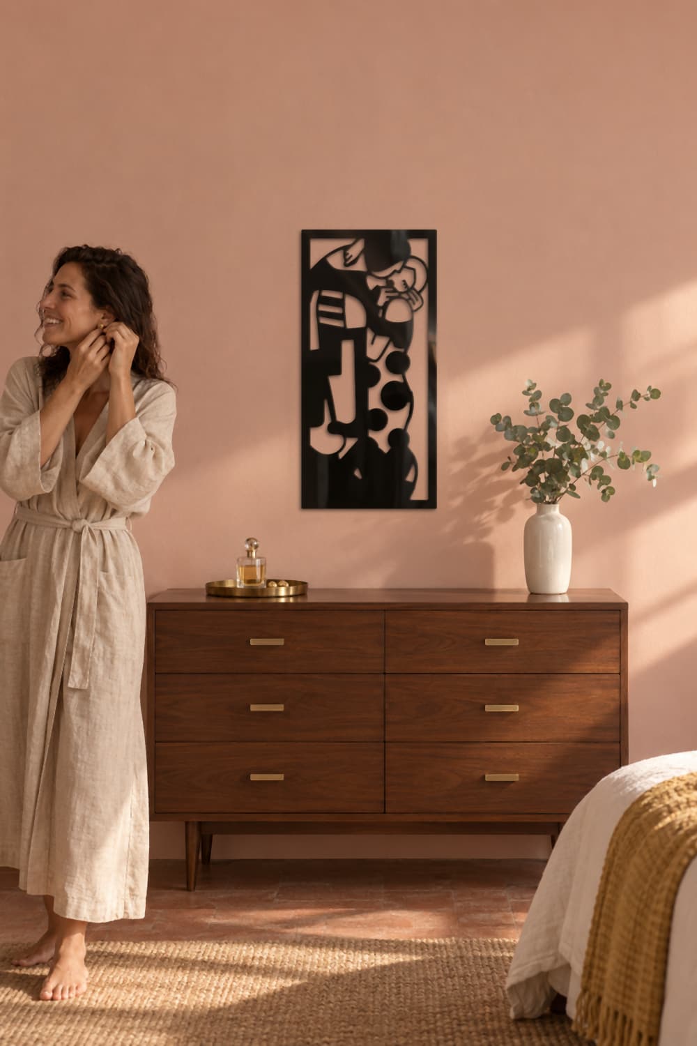 El Beso de Klimt en dormitorio rosa con cómoda de nogal y una mujer poniéndose pendientes.
